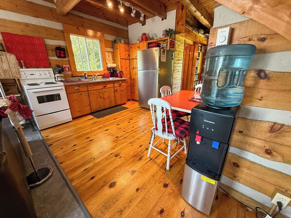 Una cocina acogedora con armarios de madera, un refrigerador de acero inoxidable, un dispensador de agua y una mesa roja.