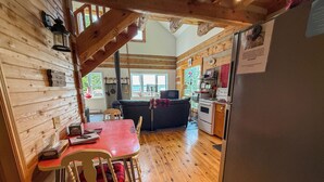 Ein gemütliches Blockhaus-Interieur mit Holzvertäfelung, einer Essecke mit rotem Tisch und einer Küche mit Herd und Kühlschrank.