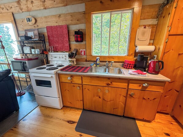 Una cocina compacta con armarios de madera, estufa, lavamanos y ventana con vista a la vegetación.