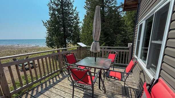 Eine Holzterrasse mit Tisch und Stühlen mit Blick auf einen Strand.
