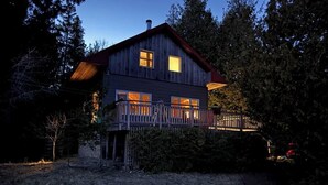 Ein Holzhaus mit Balkon und einem umzäunten Garten im Abendlicht.