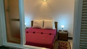 A bedroom with a bed, a nightstand, a wall-mounted light, and a window with blinds. - Villa Moon (Essaouira)