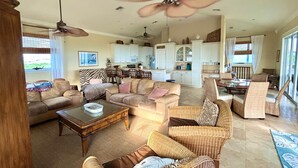 Amplia sala de estar con un ventilador de techo grande, asientos cómodos y vistas al área de cocina y comedor.