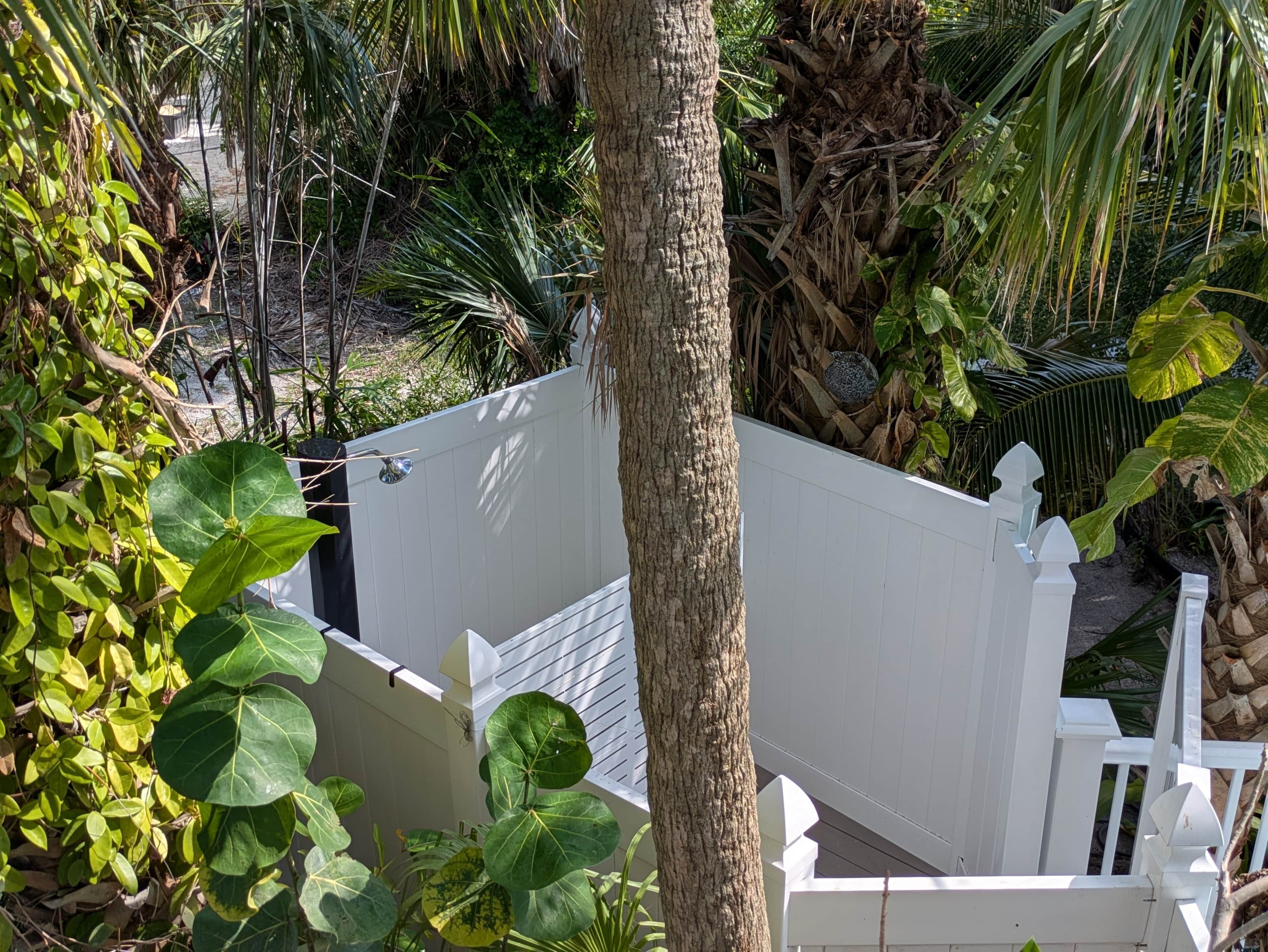 A white fence with a decorative top, surrounded by lush greenery and a tree trunk.