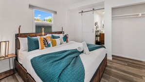 Un dormitorio moderno con cama de madera, ropa de cama azul turquesa y blanca, una ventana con vistas y un armario con puertas correderas.