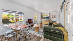 Una sala de estar moderna con un sofá verde, una mesa de comedor con sillas y un televisor.