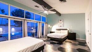 A bedroom with a large bed, a smaller bed, a nightstand, and a desk. There is a window with curtains, a ceiling fan, and a view of a swimming pool outside. - 4bd, Charming Mid-Century Home! 1.4mi to Convention Center, Mins to Strip! POOL! (Las Vegas)