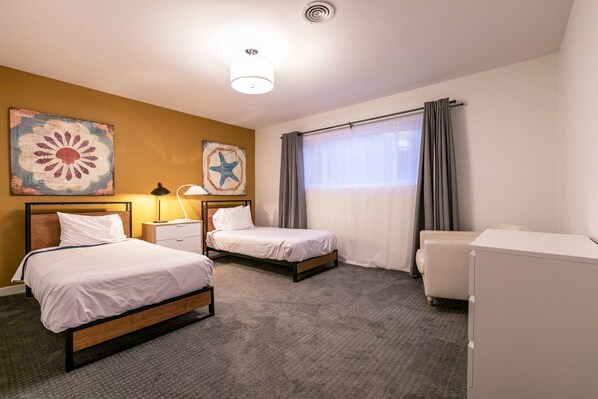 A hotel room with two single beds, a desk with a lamp, a chair, a wardrobe, and artwork on the walls. - 4bd, Charming Mid-Century Home! 1.4mi to Convention Center, Mins to Strip! POOL! (Las Vegas)