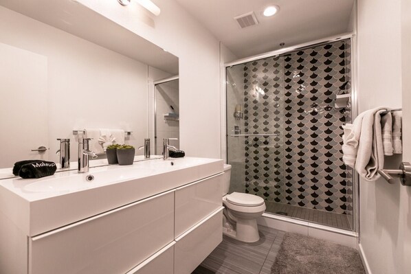 A modern bathroom with a white vanity, a large mirror, a glass shower enclosure, and a toilet. - 4bd, Charming Mid-Century Home! 1.4mi to Convention Center, Mins to Strip! POOL! (Las Vegas)