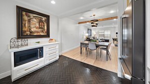 A modern kitchen with a large refrigerator, a dining area with a dark herringbone floor, and a living room with a fireplace and a large framed picture on the wall.