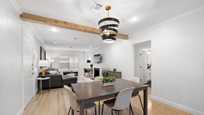 A modern living room with a dining area, wooden ceiling beams, and a fireplace.