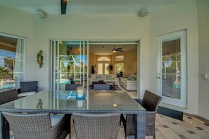A spacious dining area with a glass-top table and wicker chairs, leading to a living room with a sofa and a ceiling fan. - Palm Palace: Gulf Access Villa, Heated Pool & Spa, Sunsets (Cape Coral)
