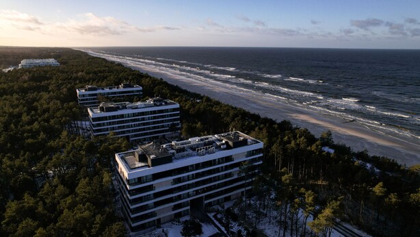 Un ensemble de bâtiments côtiers à plusieurs étages, entouré d’une forêt dense et donnant sur une plage.