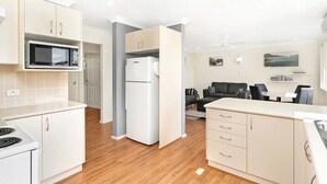 A modern kitchen with white cabinets, a microwave, a refrigerator, and a dining area with a black sofa and table.