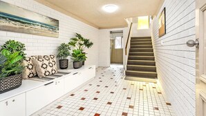 A hallway with white brick walls, a tiled floor, a staircase, and potted plants.