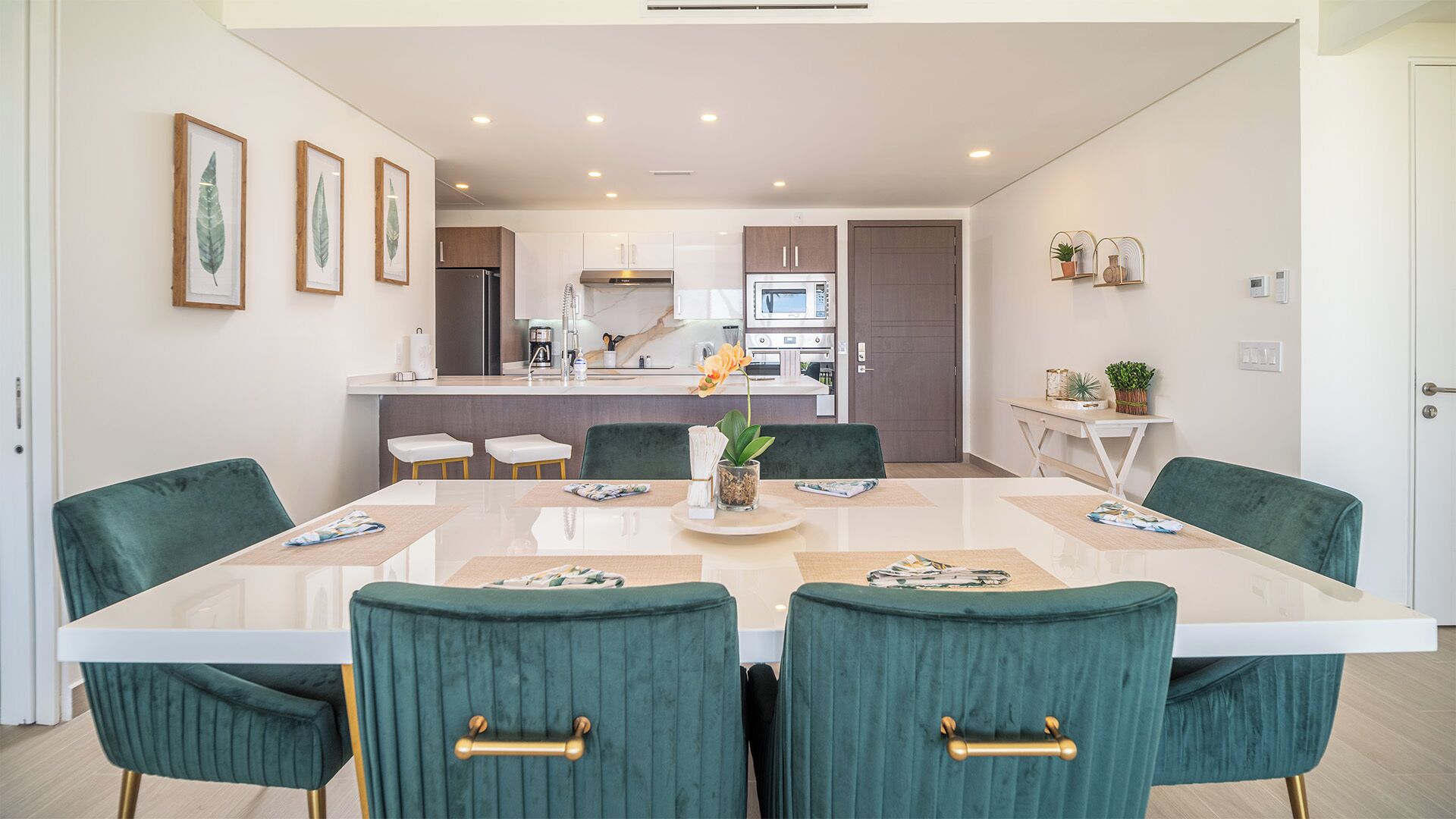 Een moderne eetruimte met een grote rechthoekige tafel, groene bekleden stoelen en een keuken op de achtergrond.