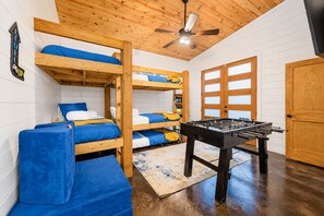 A bunk bed room with a foosball table, wooden walls, and a ceiling fan. - 1-Story Stay | Hot Tub, PingPong, Arcade & Playset (Broken Bow)