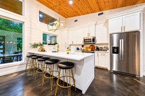 A modern kitchen with white cabinetry, stainless steel appliances, and a bar area with stools. - 1-Story Stay | Hot Tub, PingPong, Arcade & Playset (Broken Bow)