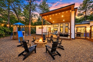 A covered outdoor seating area with a fire pit, surrounded by chairs and a play structure.