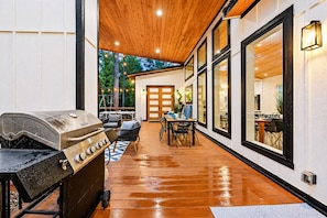 An outdoor patio with a grill, wooden flooring, and a dining area with chairs and tables.