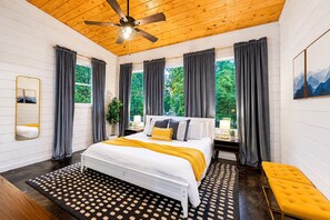 A bedroom with a bed, bedside tables, a mirror, a ceiling fan, and large windows with curtains. - 1-Story Stay | Hot Tub, PingPong, Arcade & Playset (Broken Bow)
