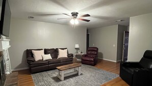 Ein Wohnzimmer mit einem braunen Ledersofa, einem Holztisch, einem roten Ledersessel und einem Deckenventilator.