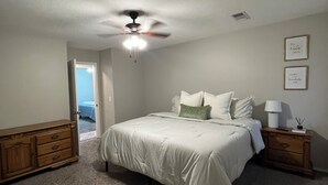 Ein Schlafzimmer mit einem Bett, einem Deckenventilator, einem Nachttisch und einer Kommode.