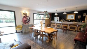 A modern kitchen with a wooden dining table and chairs, a bar area with stools, and a large window providing natural light. - Near Uzès, holiday air-conditioned villa located Vers-Pont-du-Gard, private pool. (VERS-PONT-DU-GARD)