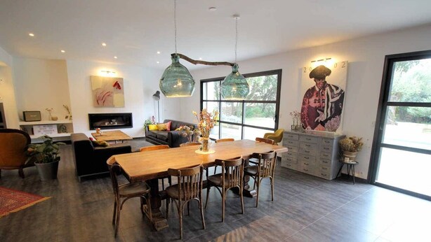 A spacious dining area with a long wooden table and chairs, a fireplace, and a large window providing natural light. - Near Uzès, holiday air-conditioned villa located Vers-Pont-du-Gard, private pool. (VERS-PONT-DU-GARD)