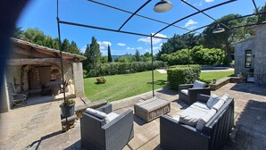 An outdoor patio with wicker furniture, a stone wall, and a view of a green lawn and trees. - Superb air-conditioned farmhouse with private pool, in Saint-Rémy-de-Provence. (SAINT-REMY-DE-PROVENCE)
