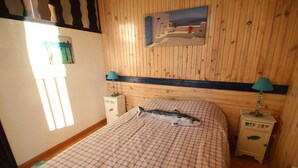 A bedroom with a wooden paneled wall, a bed with a patterned bedspread, two bedside tables with lamps, and a painting above the bed. - 0.1 ml from the beach, house with large terrace and beautiful sea view. (CARRY-LE-ROUET)