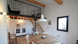 A dining area with a wooden table and white chairs, a staircase, and a loft with a black railing. - Holiday rental in Le Castellet, sea and beach 10 km. (LE CASTELLET)