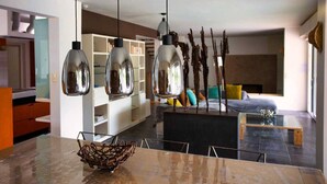 A modern living room with a glass coffee table, a sofa with cushions, and a dining area with a marble table and hanging pendant lights. - Air-conditioned villa near Vaison-la-Romaine, with heated pool. (FAUCON)