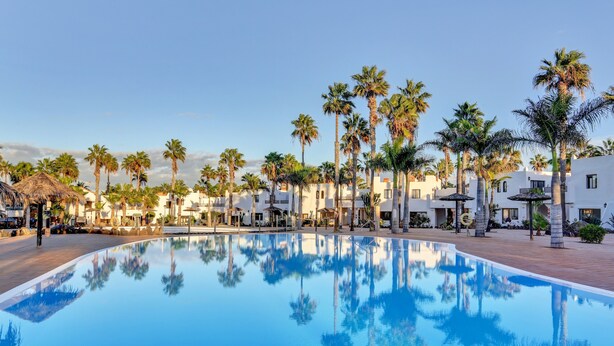 A swimming pool reflecting palm trees and white buildings. - Oasis Duna-Pistacho Dreams Pool: Shared Pool, Private Terrace & Wi-Fi (corralejo)