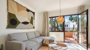 A living room with a sofa, a coffee table, a cactus, and a large abstract painting on the wall. - Oasis Duna-Pistacho Dreams Pool: Shared Pool, Private Terrace & Wi-Fi (corralejo)