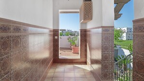 A corridor with patterned tiles, a ceiling light, and a view of a balcony with potted plants.
