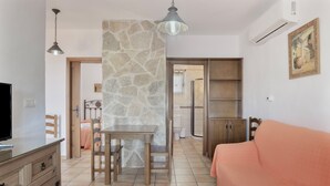 A room with a stone accent wall, a wooden dining table with chairs, a sofa, a TV, and a cabinet.
