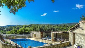 A stone pool surrounded by a white fence, with a view of a forested hillside. - Air-conditioned villa in the Luberon countryside, with fenced pool, pets allowed (2). (LIOUX)