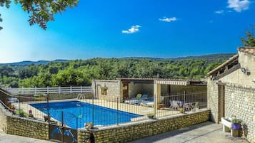 A stone pool surrounded by a white fence, with a view of a forested hillside.