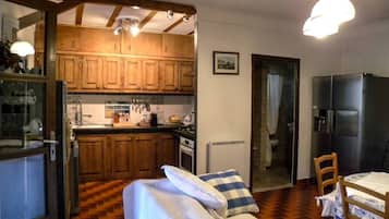A compact kitchen with wooden cabinets, a dining area with a table and chairs, and a bed with pillows.