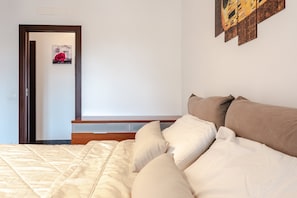 A bedroom with a bed, pillows, a wooden headboard, a nightstand, and a wall-mounted artwork.