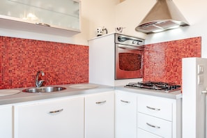 A kitchen with a double sink, stainless steel appliances, and red mosaic tile backsplash.