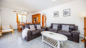 Un salon avec un canapé en cuir marron, une table basse blanche et un coin repas doté de meubles en bois.