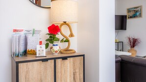 Un meuble en bois avec une lampe, un vase contenant une rose rouge et quelques documents.
