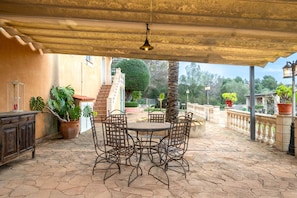 Une terrasse extérieure avec une table ronde et des chaises, des plantes en pot et une structure en forme de pergola.