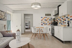 Una cocina moderna con salpicadero de azulejos, un comedor con mesa y sillas blancas, y una sala de estar con sofá y elementos decorativos.