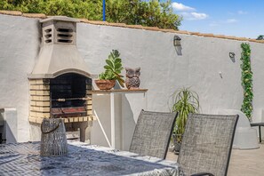 Un patio al aire libre con un horno de ladrillo, una planta en maceta, un búho decorativo y mobiliario de exterior.