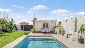 A swimming pool with a patio area, a small table with chairs, and potted plants.