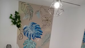 Un dormitorio con cama, ropa de cama blanca, una pared con un mural floral, un candelabro colgante y una mesita de noche con lámpara.