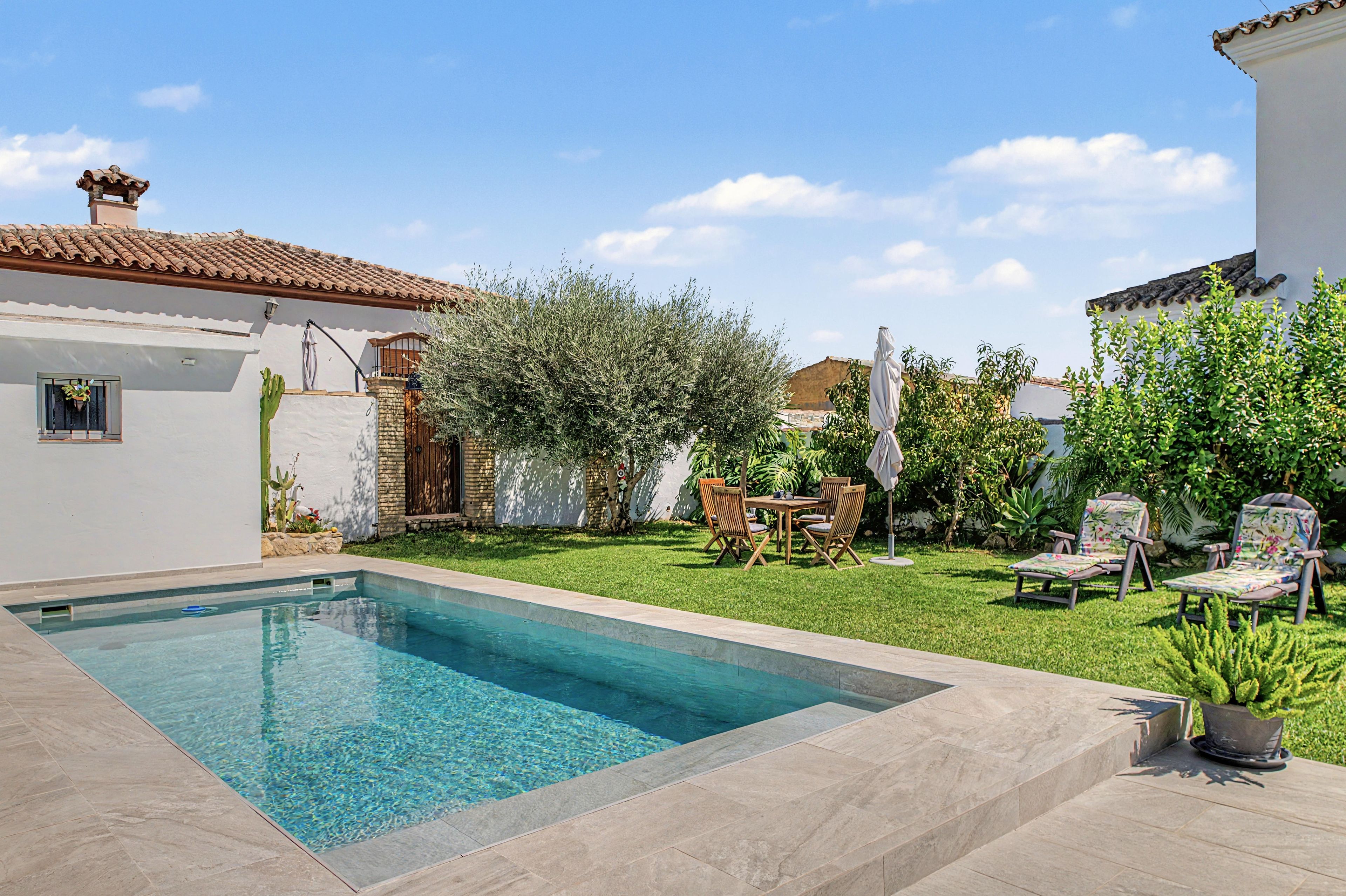 Una piscina con solárium de baldosas, césped y un patio con mobiliario exterior.